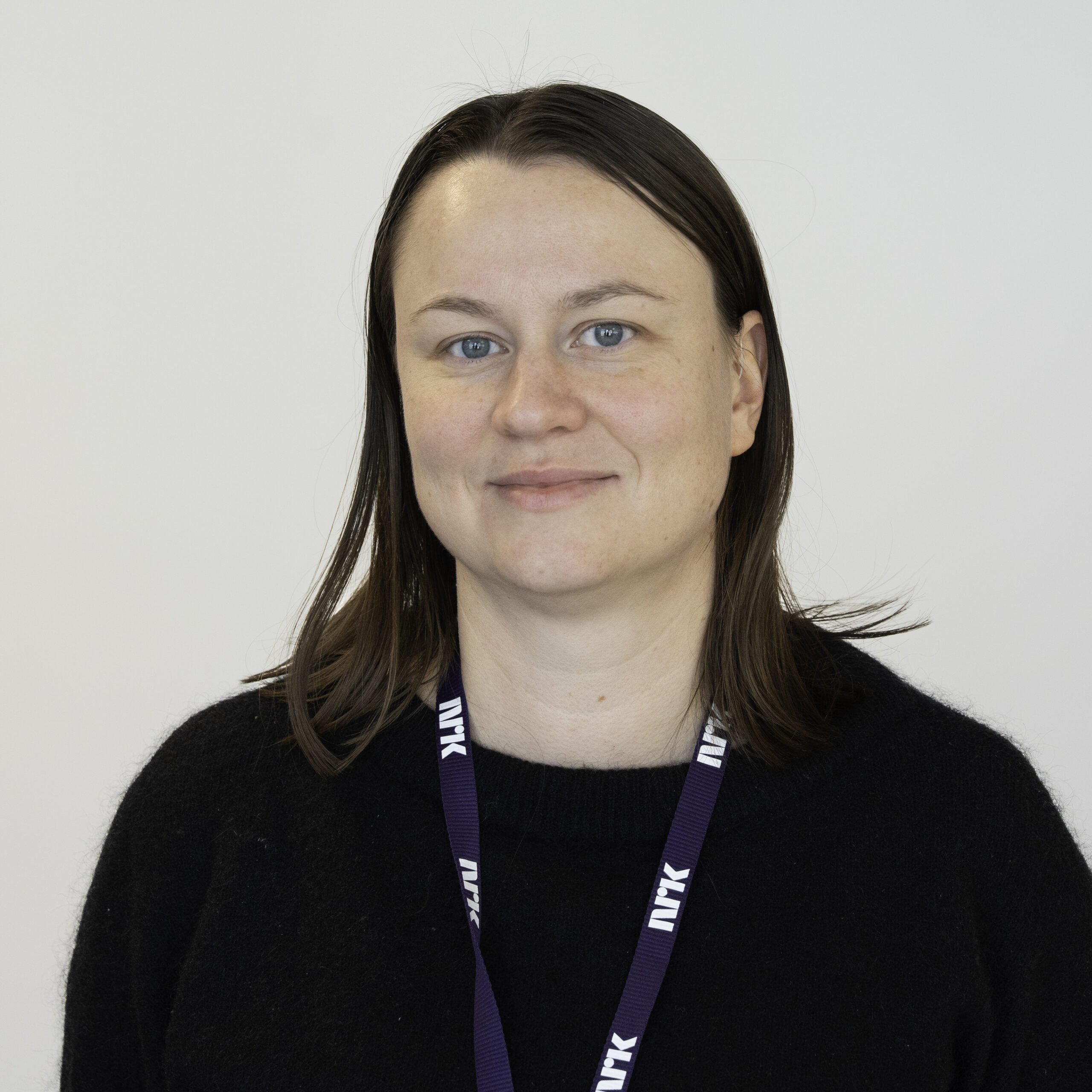 Dette er et portrettbilde av Camilla Gjerde Lund. Hun ser rett mot kamera. Hun har halvlangt mørkt hår som går ned over skuldrene. Hun har på seg en blåaktig genser. Rundt halsen har hun snora til et nøkkel- eller adgangskort.