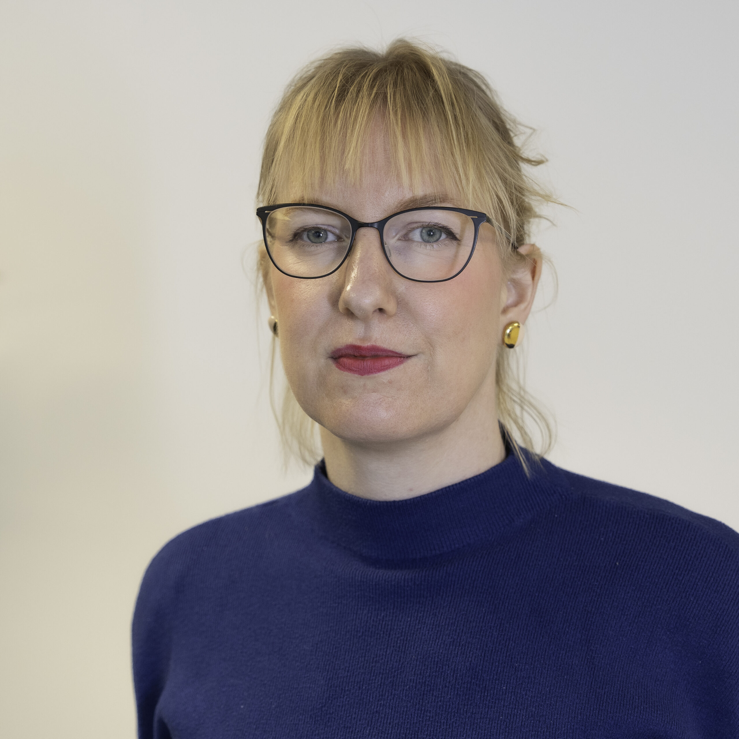 Bildet viser Marit Henriette Gustavsen. Hun har lyst, halvlangt hår og briller. Hun ser rett i kamera med munnet lukket. Hun har på seg en blåaktig genser. 